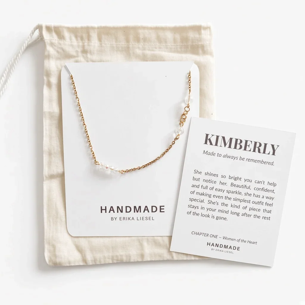 A delicate gold chain necklace with small clear beads, displayed on a white card next to a cream fabric drawstring bag and a printed gift message card. The brand HANDMADE BY ERIKA LIESEL is visible on the card.