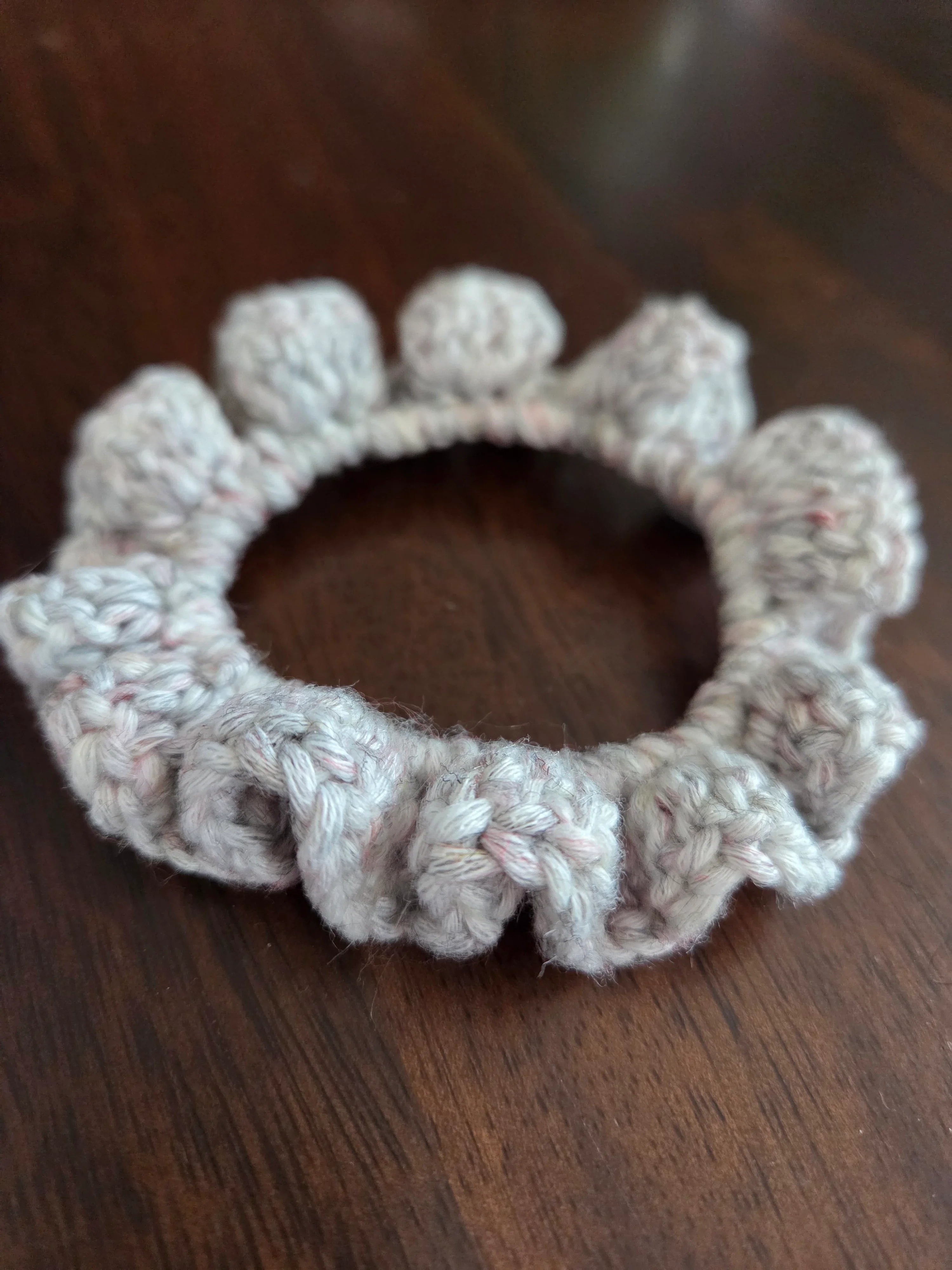 Handmade crochet scrunchie with bobble edge on a dark wood table