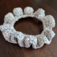 Handmade crochet scrunchie with bobble edge on a dark wood table