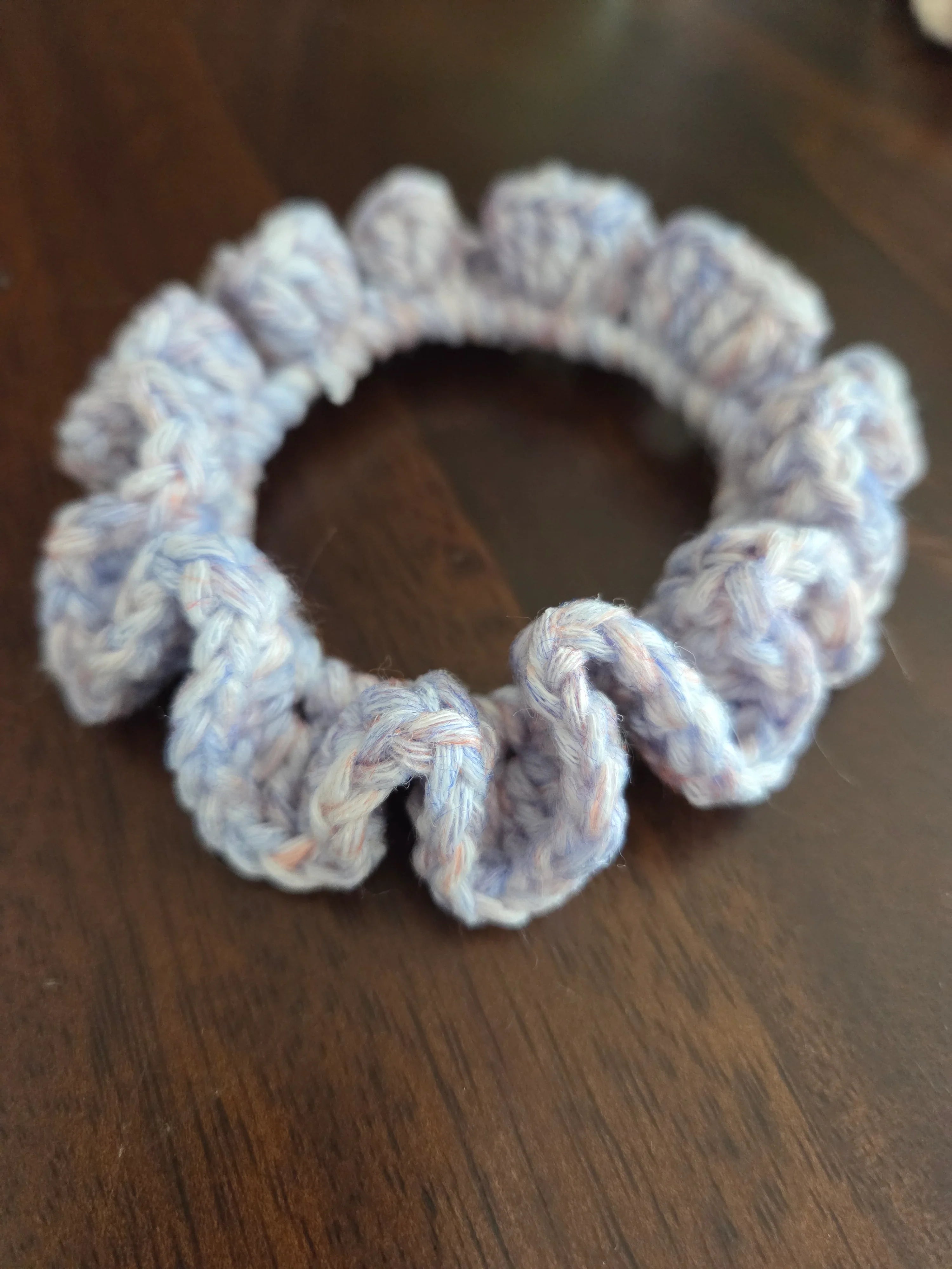 Light purple crocheted hair scrunchie on a dark wooden surface