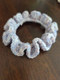 Light purple crocheted hair scrunchie on a dark wooden surface