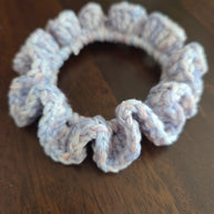 Light purple crocheted hair scrunchie on a dark wooden surface