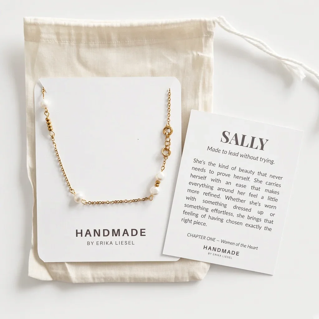 A delicate gold chain necklace with small white pearl-like beads and a gold oval charm, displayed on a white card next to a printed message card and a cream fabric pouch. The brand name 'HANDMADE BY ERIKA LIESEL' is visible on the packaging.