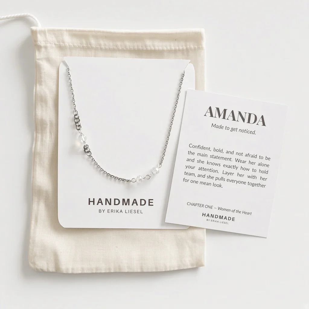 A delicate silver chain necklace with small clear beads and a central white pearl pendant, displayed on a white card next to a cream fabric pouch and a printed card reading 'AMANDA Made to get noticed.'.