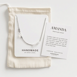 A delicate silver chain necklace with small clear beads and a central white pearl pendant, displayed on a white card next to a cream fabric pouch and a printed card reading 'AMANDA Made to get noticed.'.