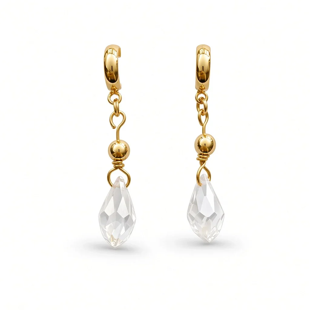 A pair of gold huggie hoop earrings with dangling chains, small gold beads, and clear faceted teardrop crystal drops, shown on a clean white background.