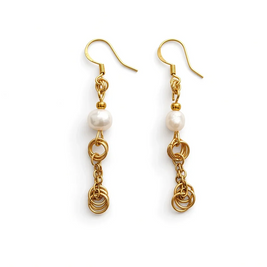 A pair of gold dangle earrings with a white pearl bead and intricate gold chain and ring details, shown on a plain white background.