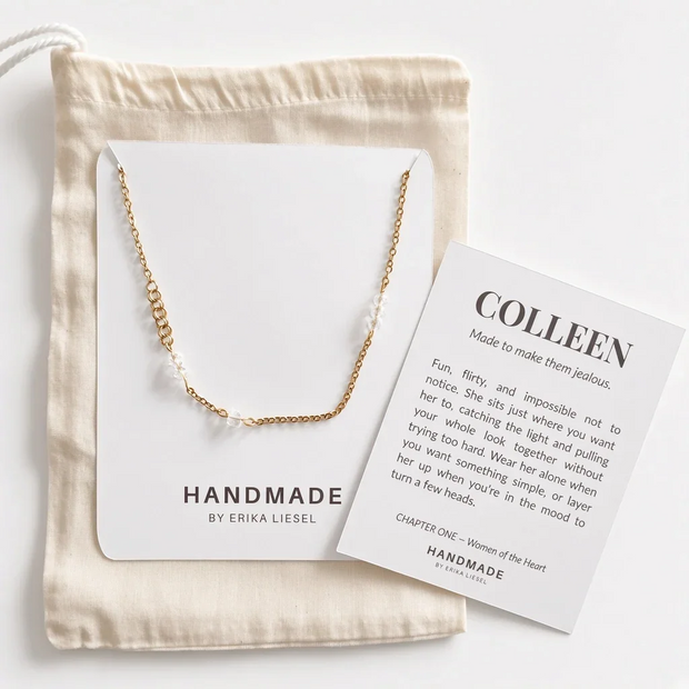 A delicate gold chain necklace is displayed on a white card next to a beige fabric drawstring bag and a printed insert card reading 'COLLEEN' by Handmade by Erika Liesel, arranged on a light neutral background.