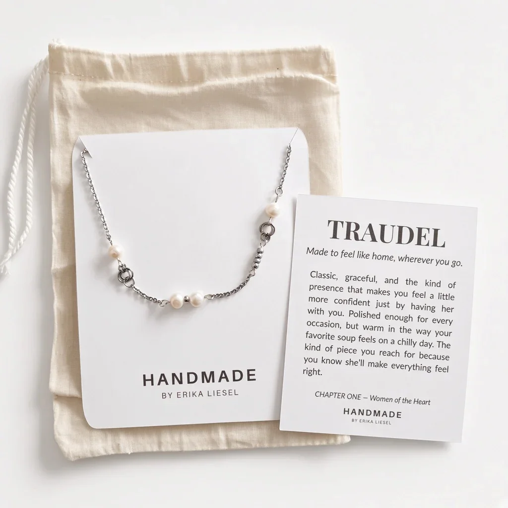 A silver and white bead necklace from Handmade by Erika Liesel is displayed on a white card next to a beige drawstring pouch and a printed message card titled 'TRAUEDEL'.