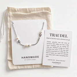 A silver and white bead necklace from Handmade by Erika Liesel is displayed on a white card next to a beige drawstring pouch and a printed message card titled 'TRAUEDEL'.