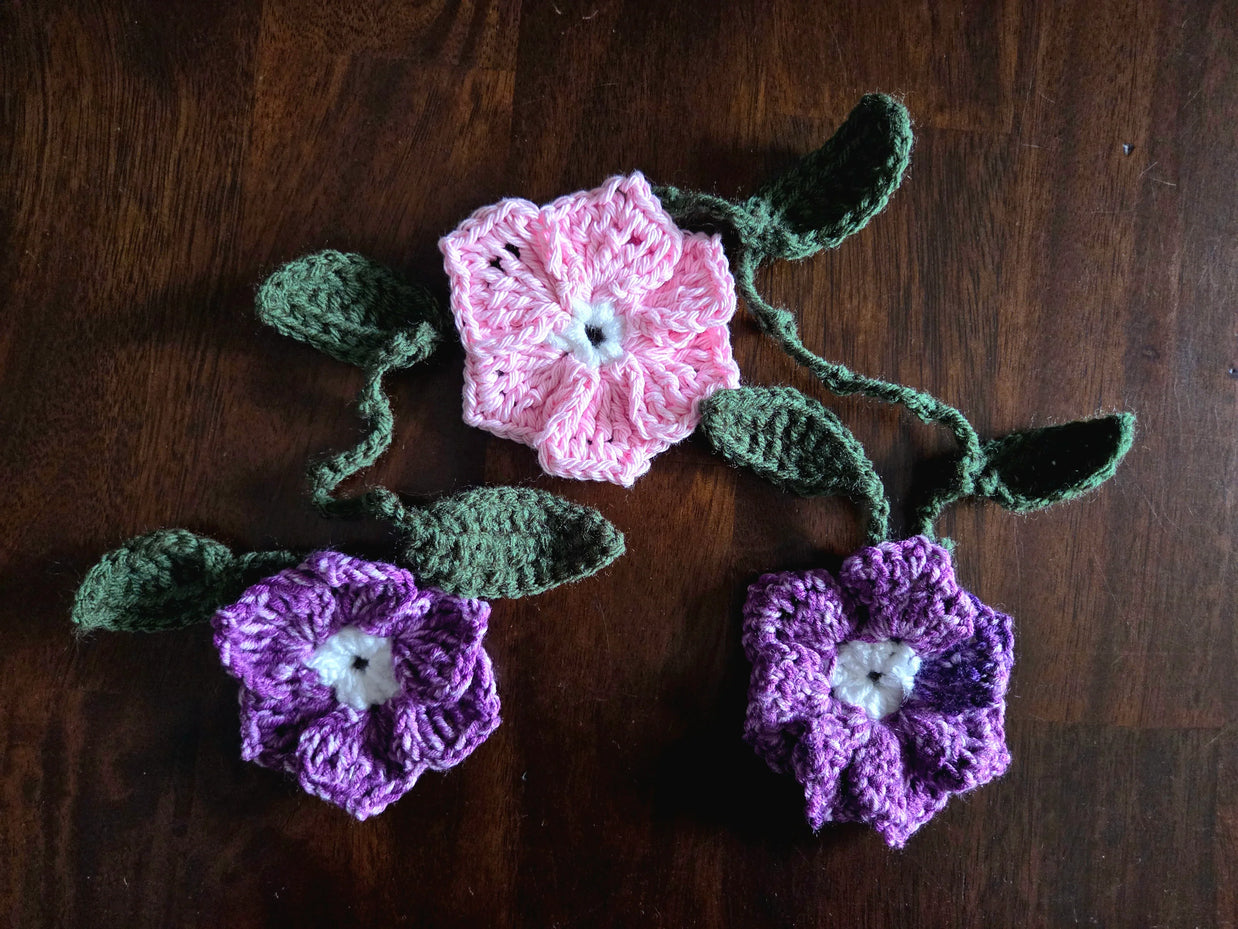 Three crocheted flowers, two pink and one purple, on a wooden surface.