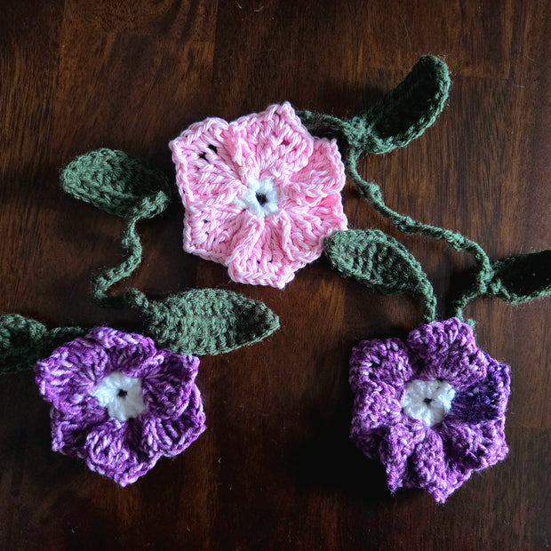 Three crocheted flowers, two pink and one purple, on a wooden surface.