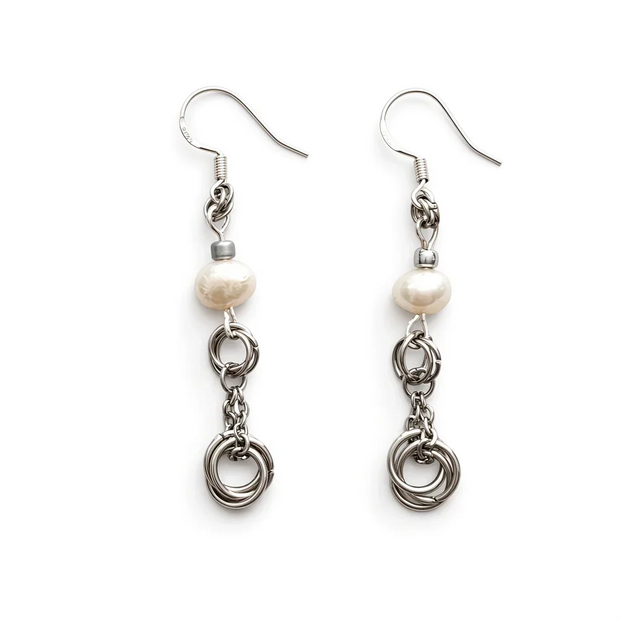 A pair of silver-toned dangle earrings with a single irregular white freshwater pearl and three interlinked silver rings, shown on a plain white background.