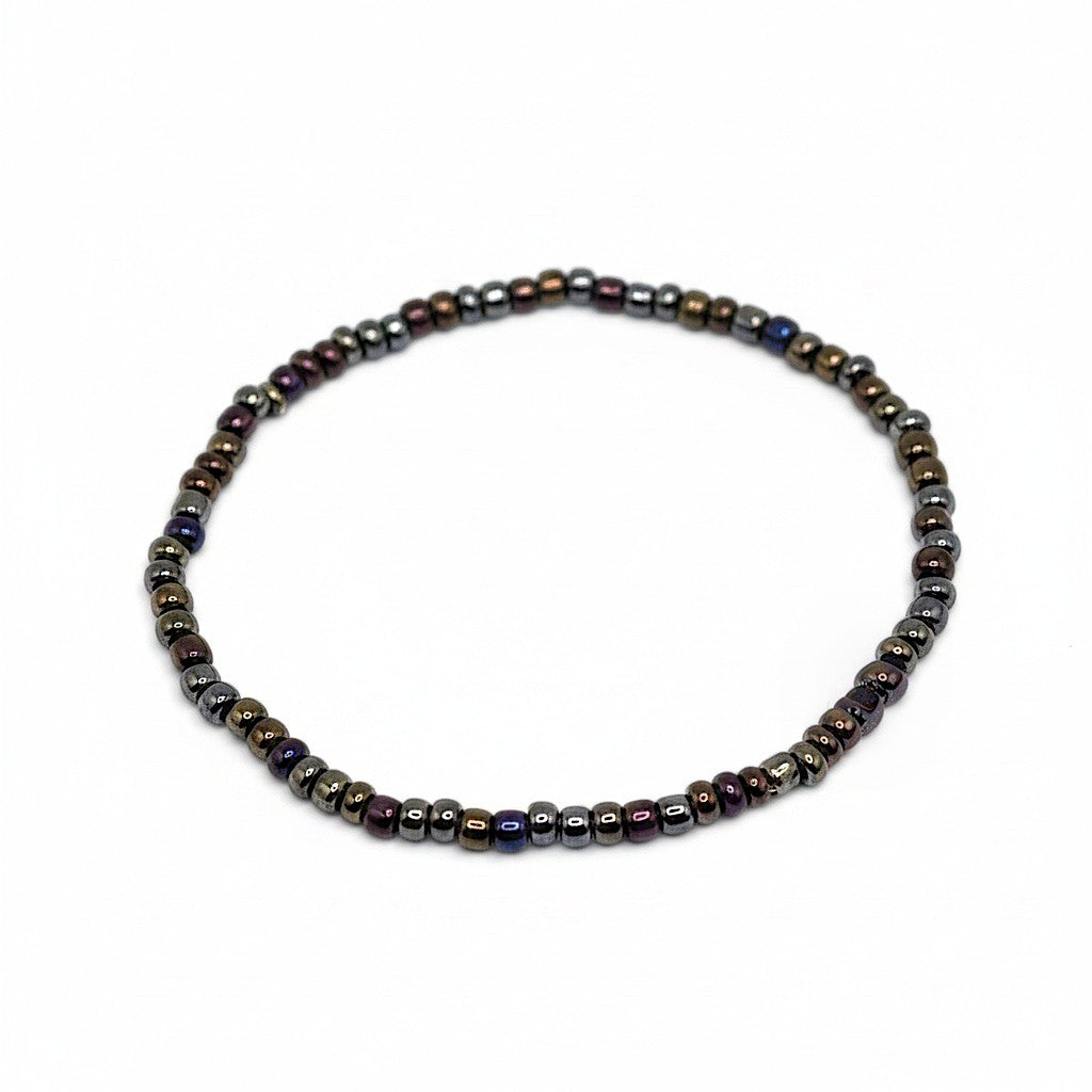 Handmade by Erika Liesel Aurora stretch bracelet featuring dark iridescent glass beads in bronze, purple, and blue.