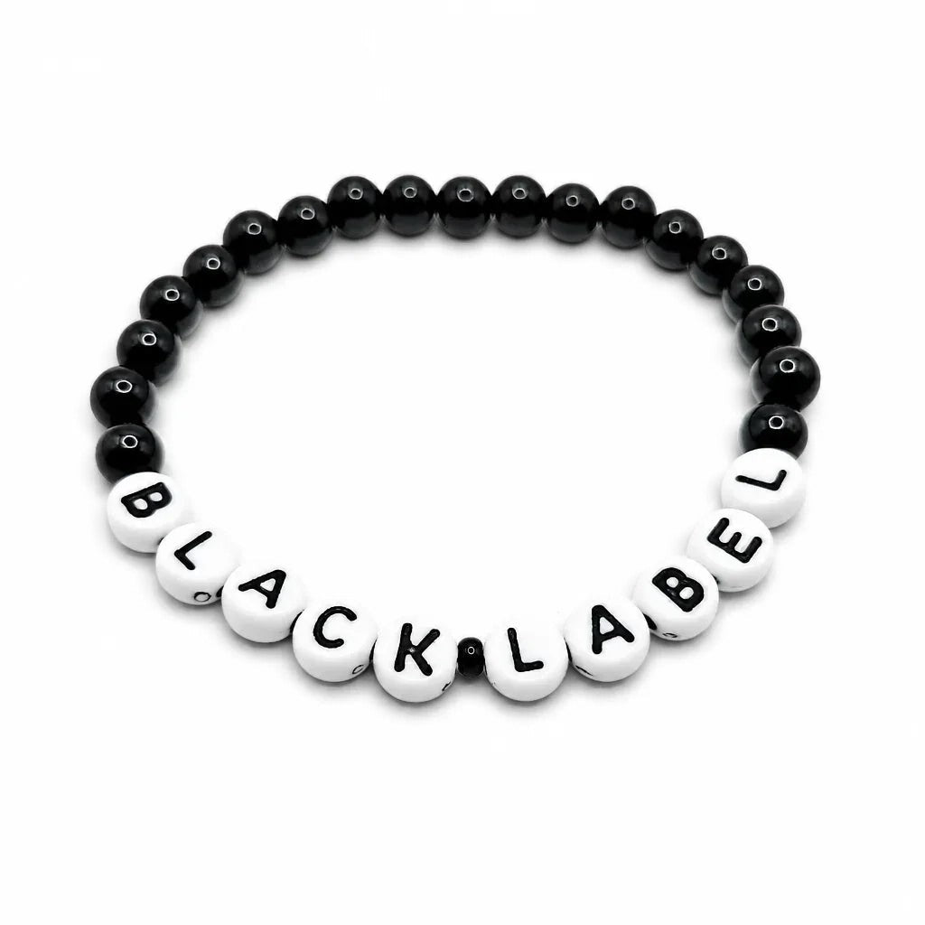 Handmade by Erika Liesel Black Label stretch bracelet with black glass beads and white letter beads on white background
