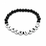 Handmade by Erika Liesel Black Label stretch bracelet with black glass beads and white letter beads on white background