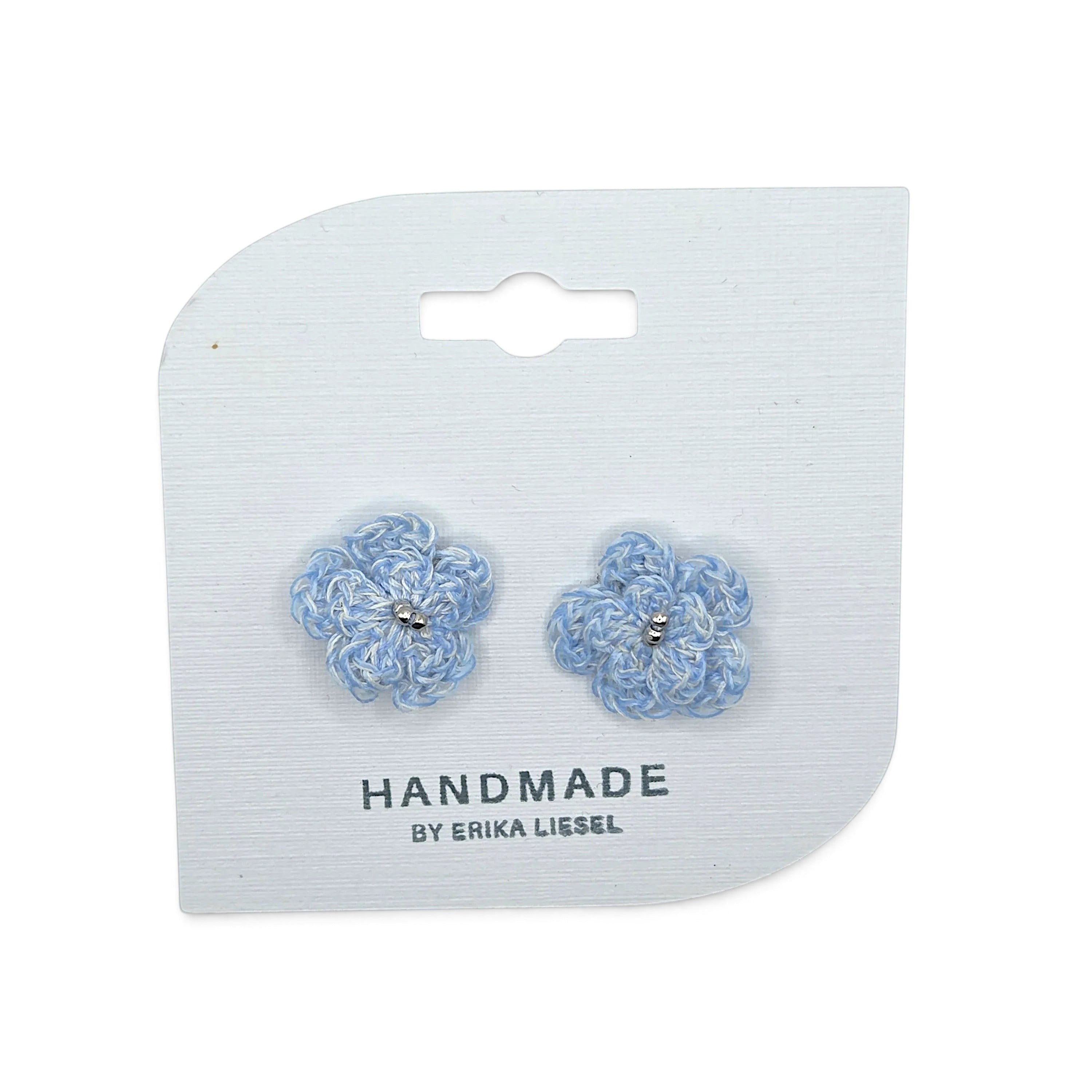 Handmade by Erika Liesel Bloom crochet flower earrings in light blue with silver bead accents on a display card.
