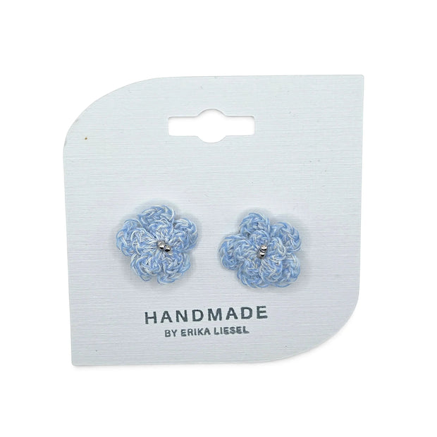 Handmade by Erika Liesel Bloom crochet flower earrings in light blue with silver bead accents on a display card.