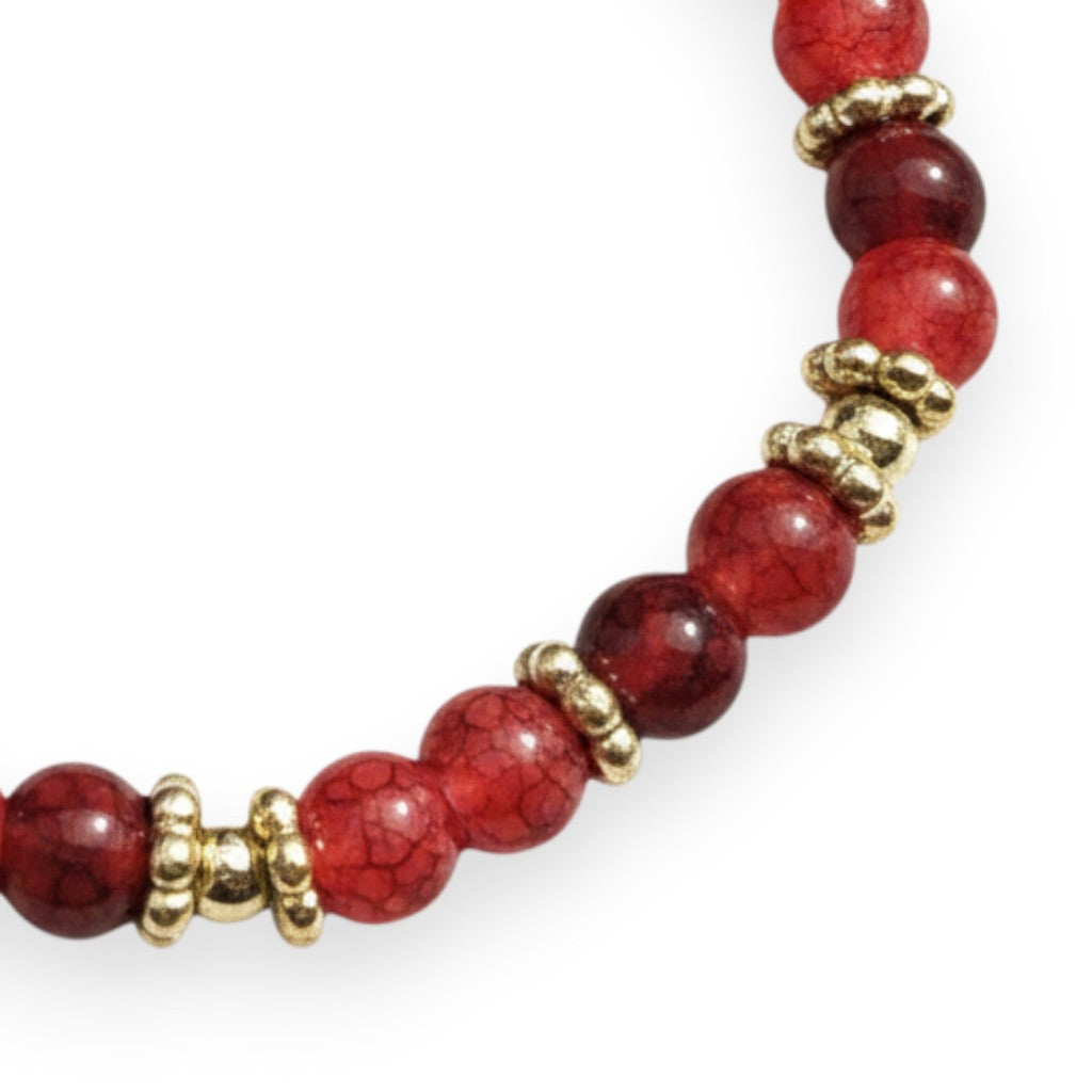 Handmade by Erika Liesel crimson glass bead stretch bracelet with polished gold spacers on a white background.