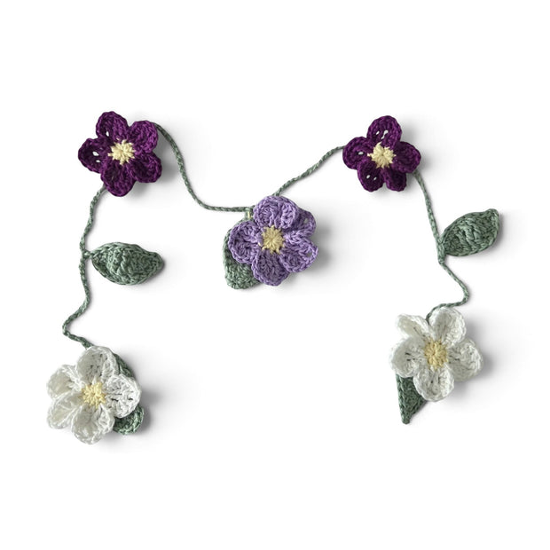 Handmade by Erika Liesel crochet floral garland featuring purple, lavender, and white flowers with green leaves.
