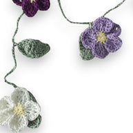 Handmade by Erika Liesel crochet floral garland featuring purple, lavender, and white flowers with green leaves.
