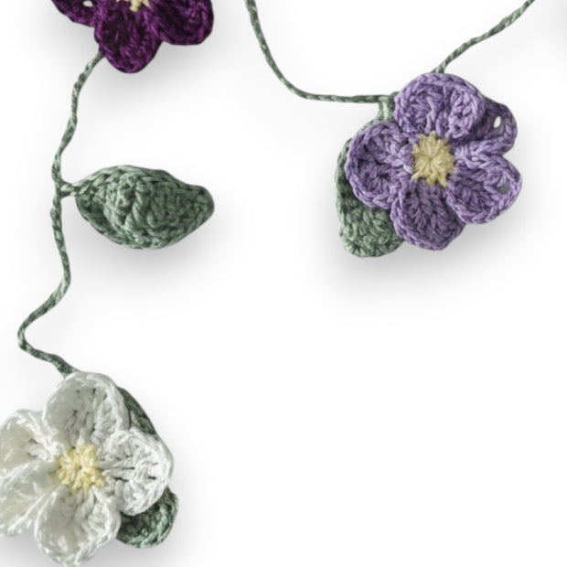 Handmade by Erika Liesel crochet floral garland featuring purple, lavender, and white flowers with green leaves.