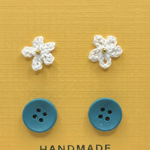Handmade by Erika Liesel Cute-As-A-Button set featuring white crocheted flower studs and blue button stud earrings.