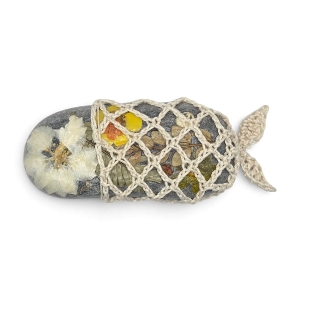 Handmade by Erika Liesel crochet stone sleeve featuring a fish-shaped design with dried flowers on a natural stone.