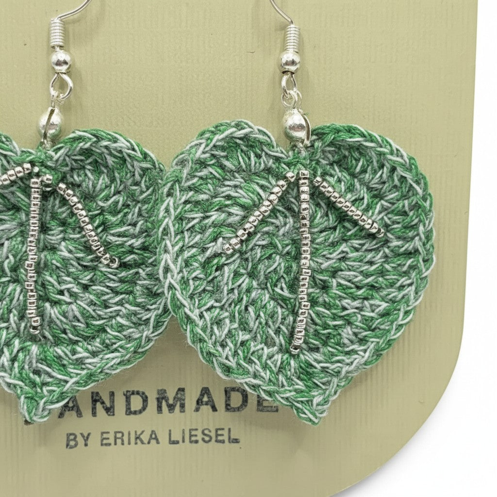 Handmade by Erika Liesel green crochet leaf earrings with silver glass bead accents on a display card.