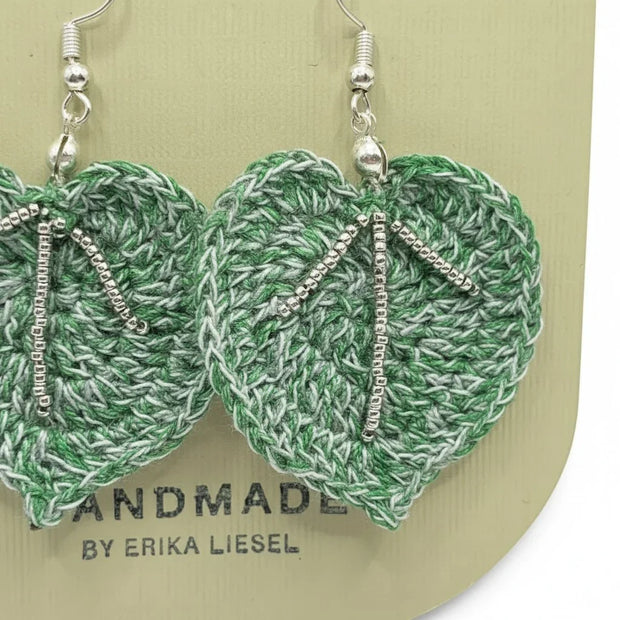 Handmade by Erika Liesel green crochet leaf earrings with silver glass bead accents on a display card.