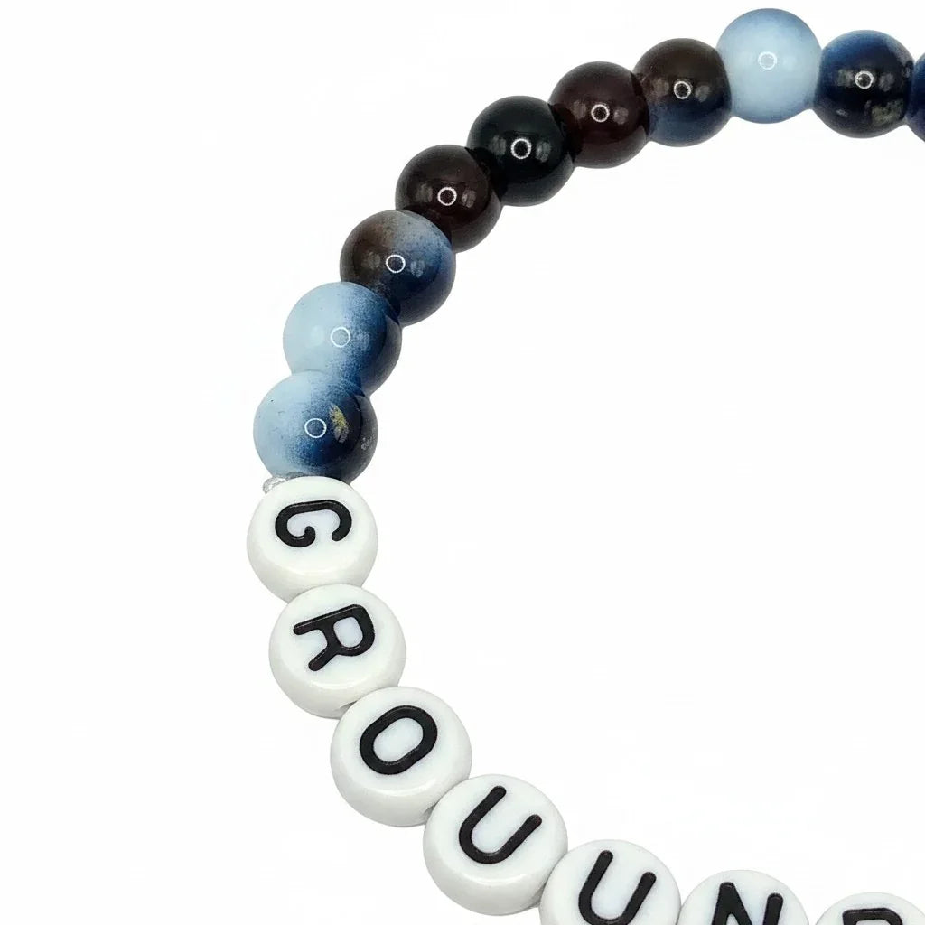 Handmade by Erika Liesel Grounded stretch bracelet featuring dark blue and brown 6mm glass beads with lettered charms.
