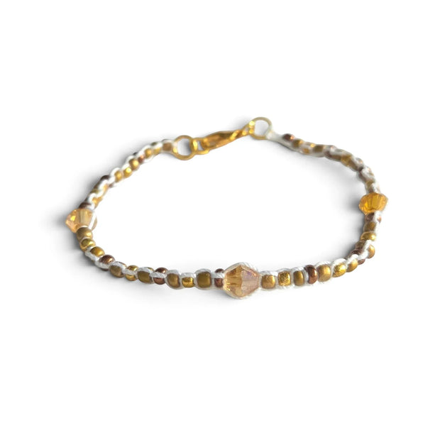 Handmade beaded bracelet with gold and amber crystals, white cord, and gold clasp on white fabric