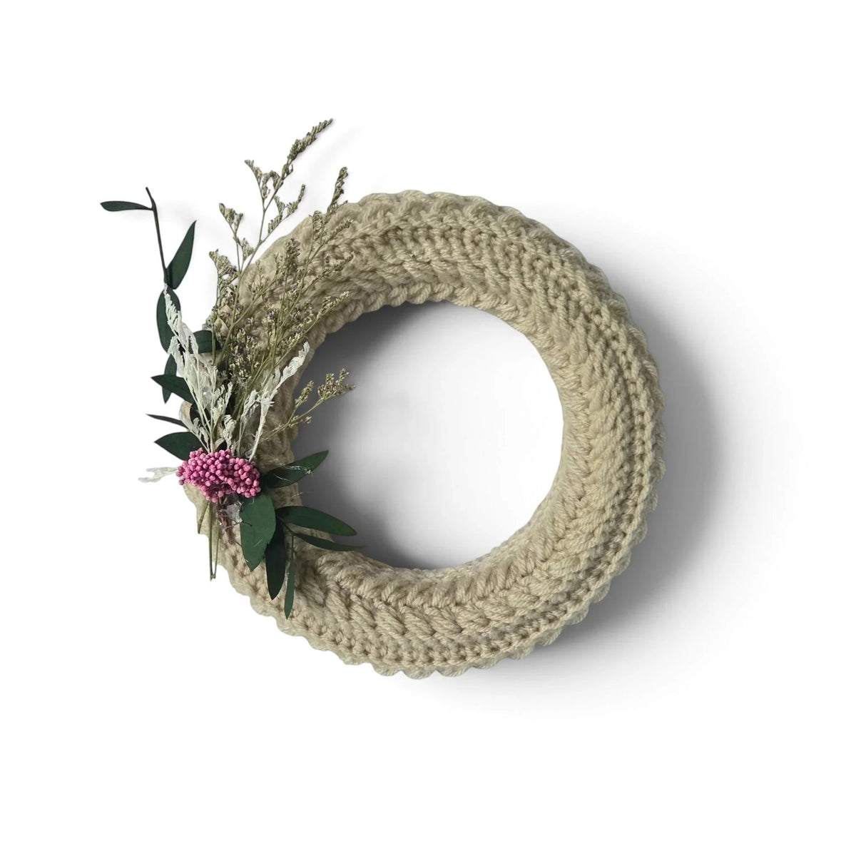 Handmade by Erika Liesel small crochet wreath in neutral beige yarn with dried floral accents on a white background.