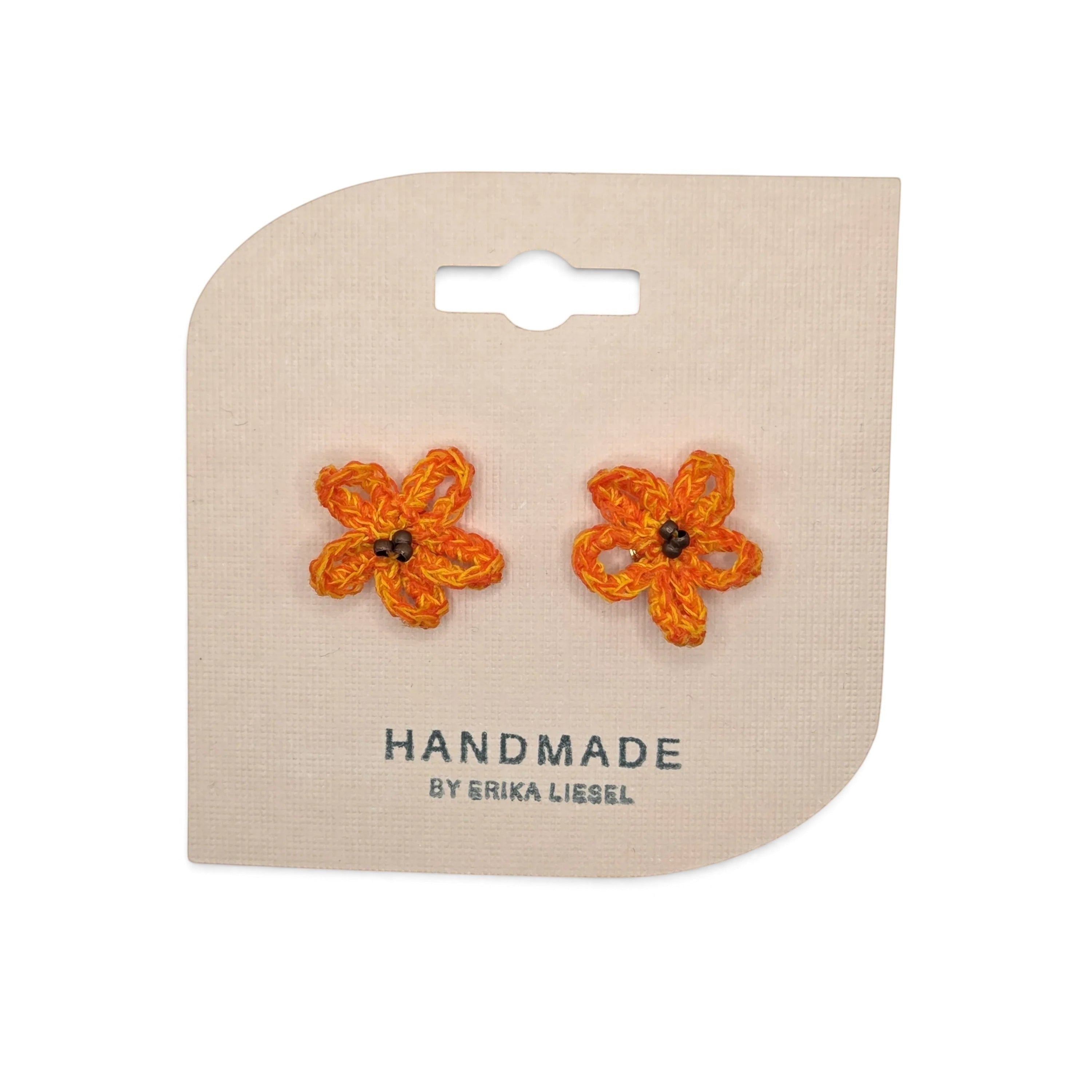 Handmade by Erika Liesel orange daisy bud crochet stud earrings with glass bead centers on a branded display card.