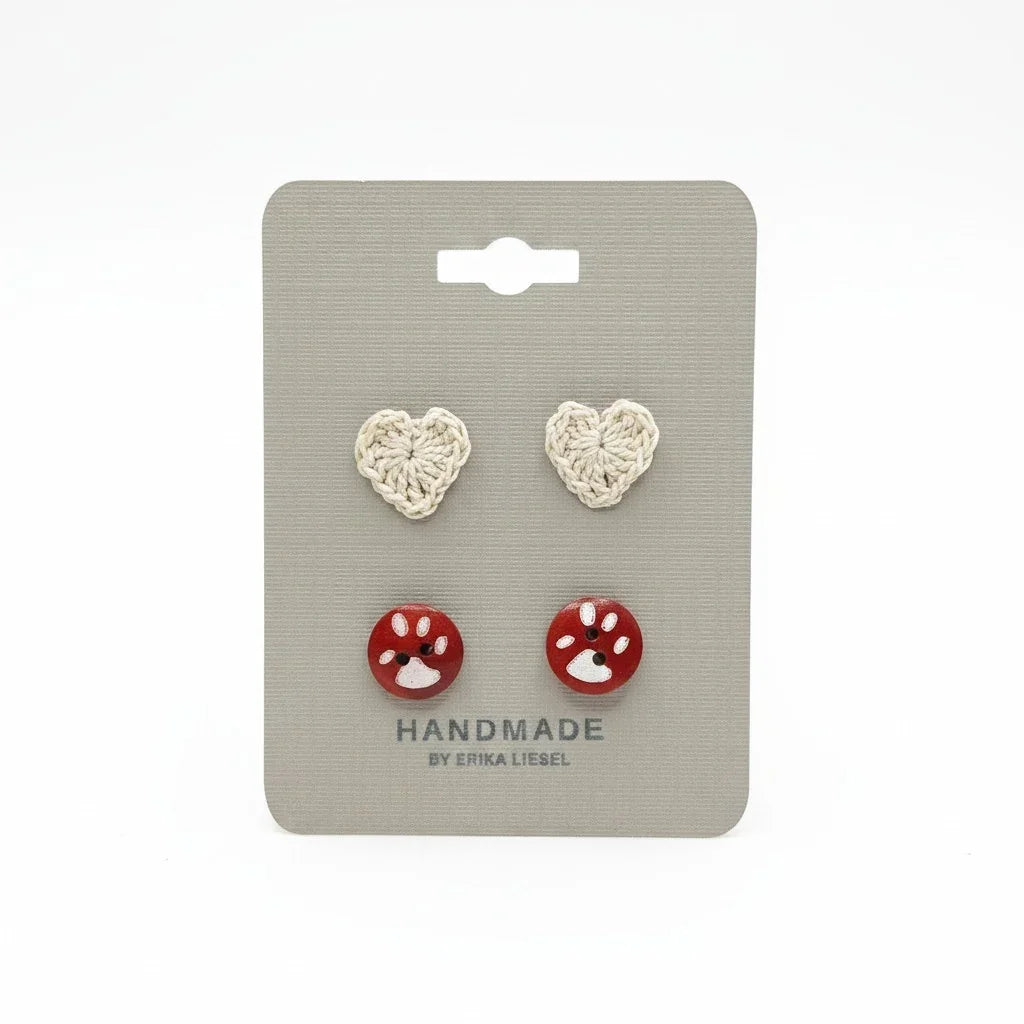 Handmade by Erika Liesel paw print button studs and crochet heart stud earrings on a grey display card.