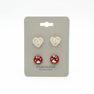 Handmade by Erika Liesel paw print button studs and crochet heart stud earrings on a grey display card.