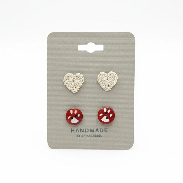 Handmade by Erika Liesel paw print button studs and crochet heart stud earrings on a grey display card.