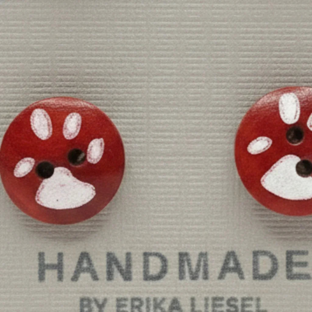 Handmade by Erika Liesel paw print button studs and cream crochet heart stud earrings on a display card.