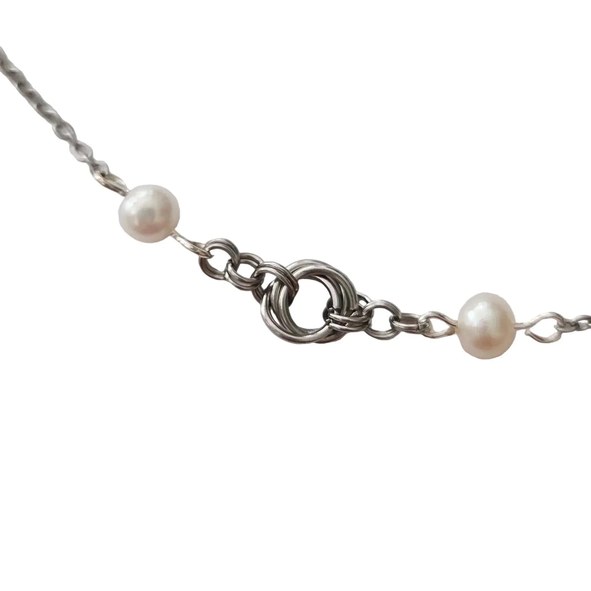A close-up of a silver chain necklace featuring two small, round, off-white pearl beads and a central silver ring clasp, set against a plain light gray background.
