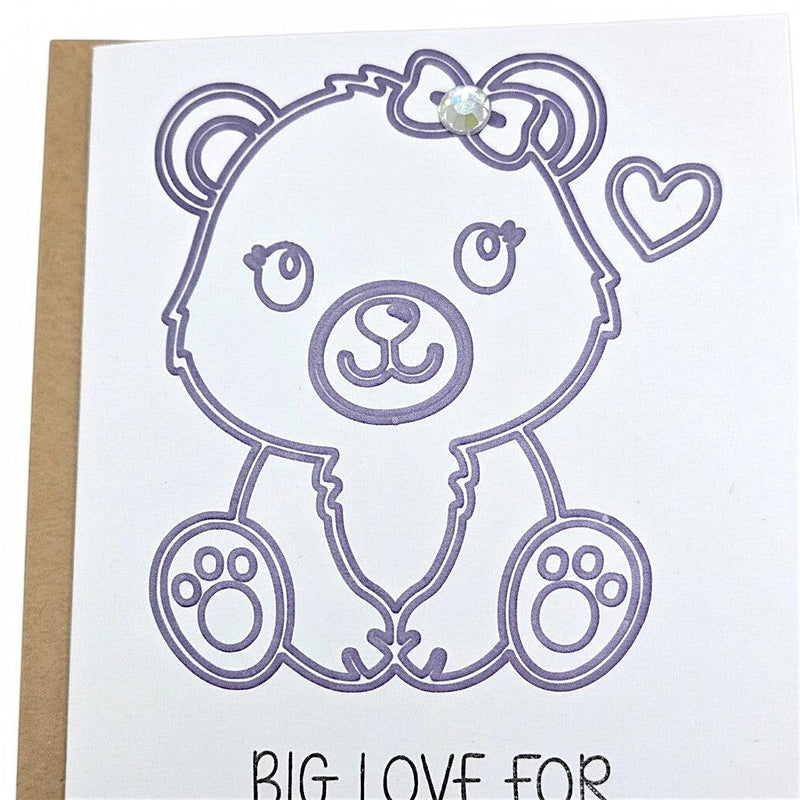 Handmade by Erika Liesel baby card featuring a purple outline of a cute bear with a sparkly gem bow and heart detail.