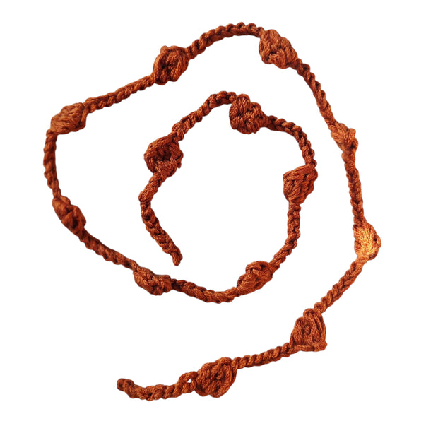 Handmade by Erika Liesel rust-colored crochet garland with textured knots for cozy home decor and shelf styling.