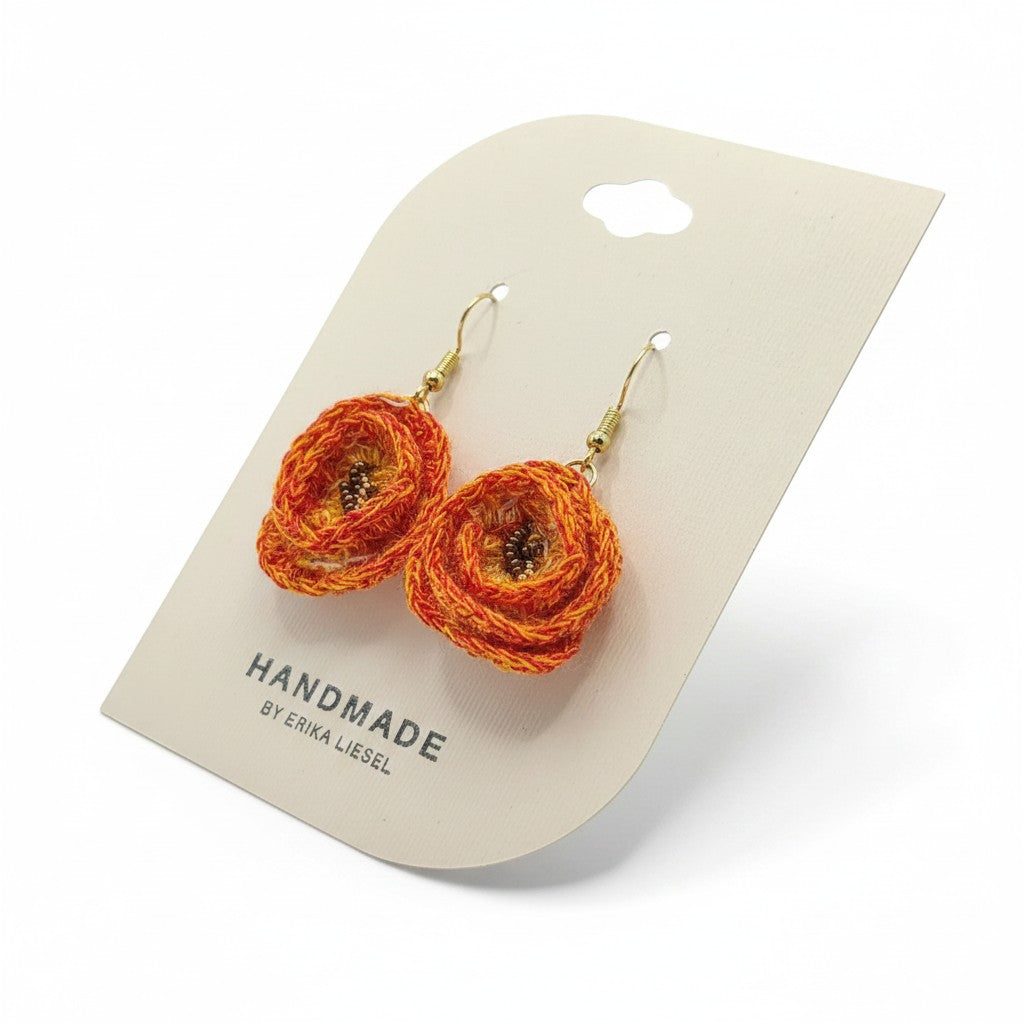 Handmade by Erika Liesel tangerine orange crochet flower earrings with gold hooks and glass bead centers on display.