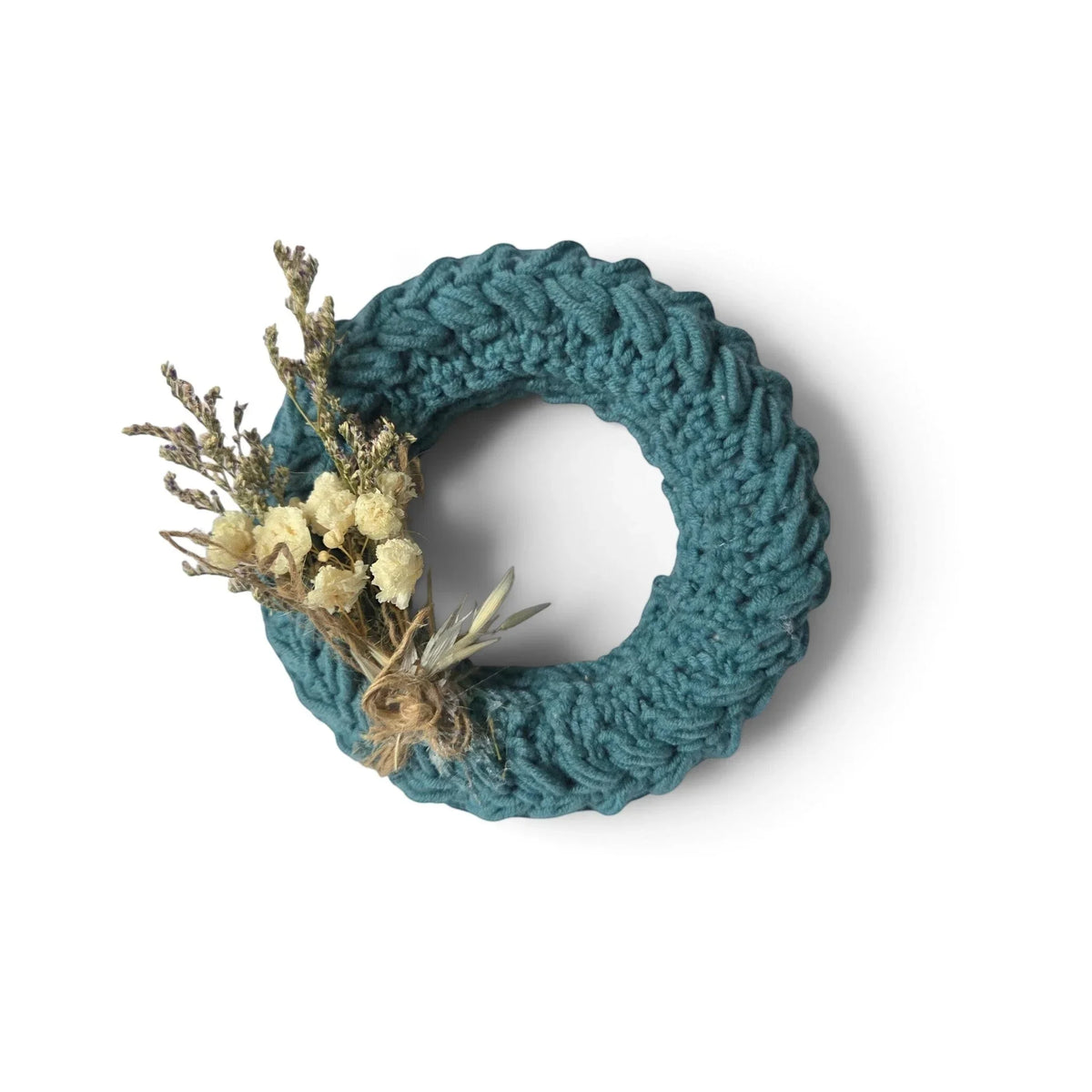 Handmade by Erika Liesel mini teal crochet wreath decorated with dried flowers on a neutral fabric background