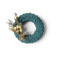 Handmade by Erika Liesel mini teal crochet wreath decorated with dried flowers on a neutral fabric background