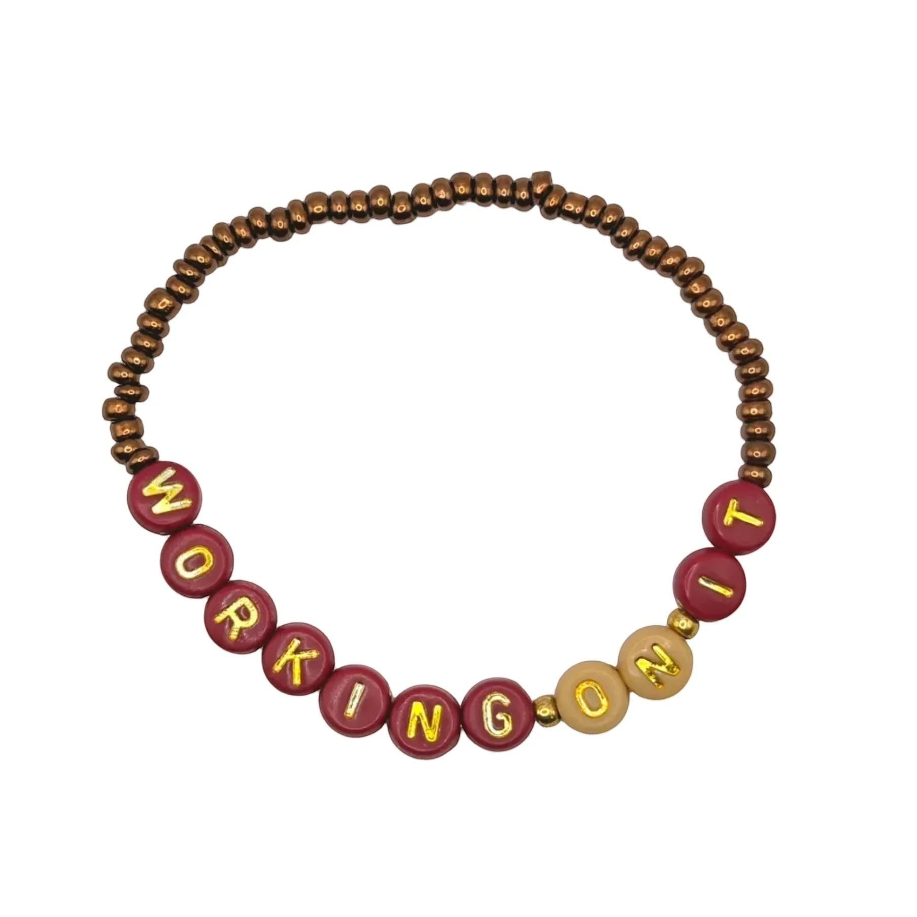 Handmade by Erika Liesel Working On It stretch bracelet with 4mm glass beads, gold-foil letters, and gold accents.