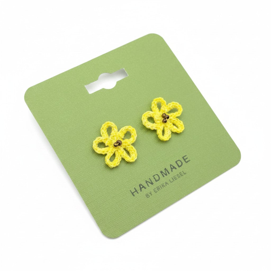 Handmade by Erika Liesel yellow daisy crochet stud earrings with glass bead centers on a green display card.
