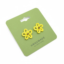 Handmade by Erika Liesel yellow daisy crochet stud earrings with glass bead centers on a green display card.