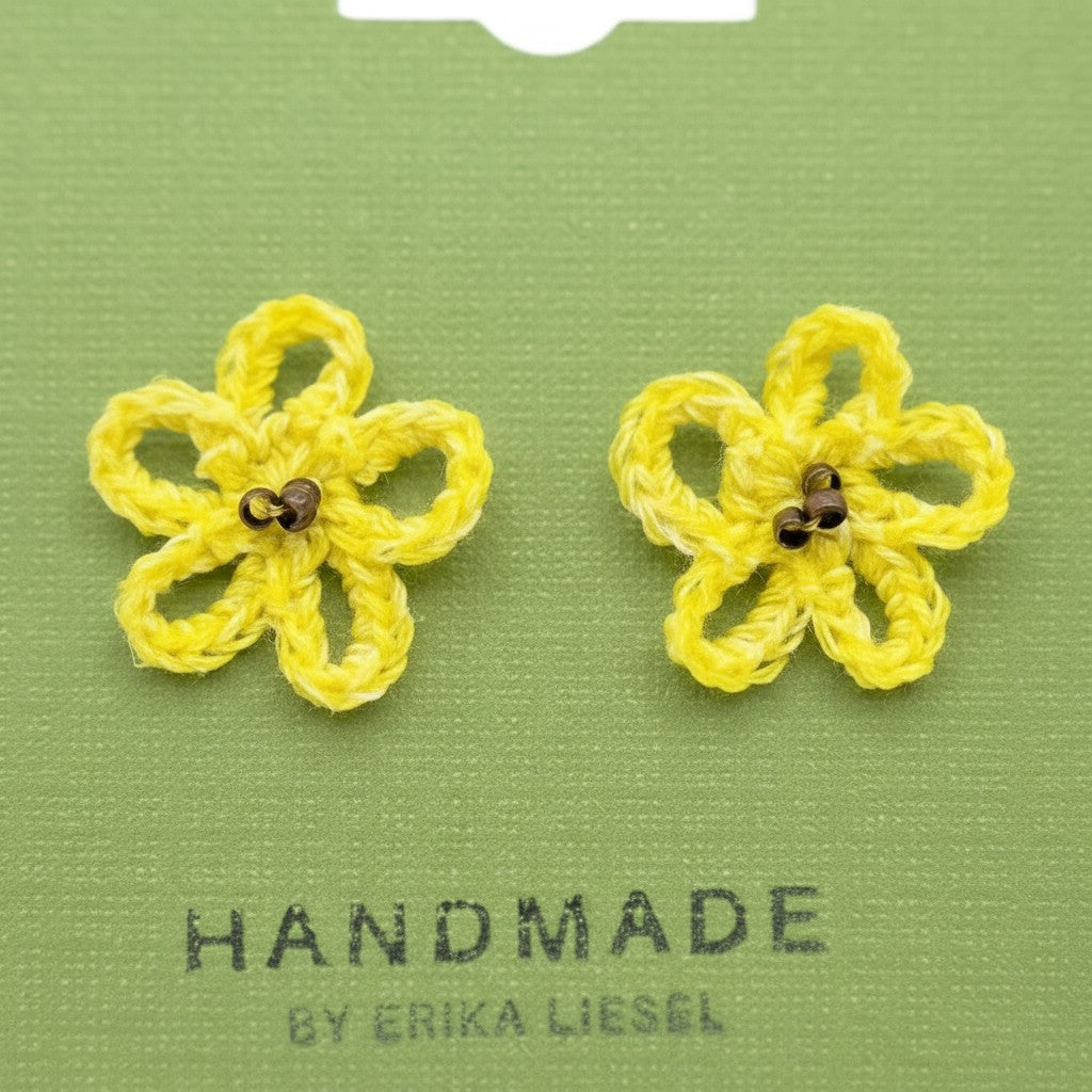 Handmade by Erika Liesel yellow crochet daisy stud earrings with glass bead centers on a green display card.