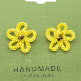Handmade by Erika Liesel yellow crochet daisy stud earrings with glass bead centers on a green display card.