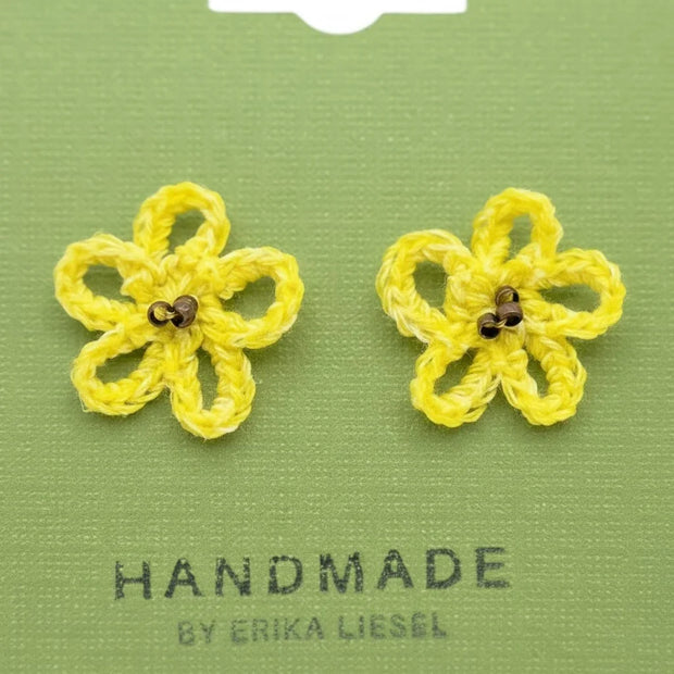 Handmade by Erika Liesel yellow crochet daisy stud earrings with glass bead centers on a green display card.